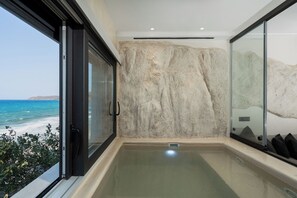 A modern bathroom with a large glass door, a view of the sea, and a stone wall.