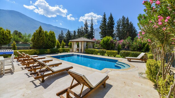 A pool area with lounge chairs, a gazebo, and a mountain backdrop.