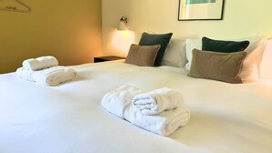 Une chambre d’hôtel avec un lit, des oreillers, une table de chevet, une lampe fixée au mur et un tableau encadré.