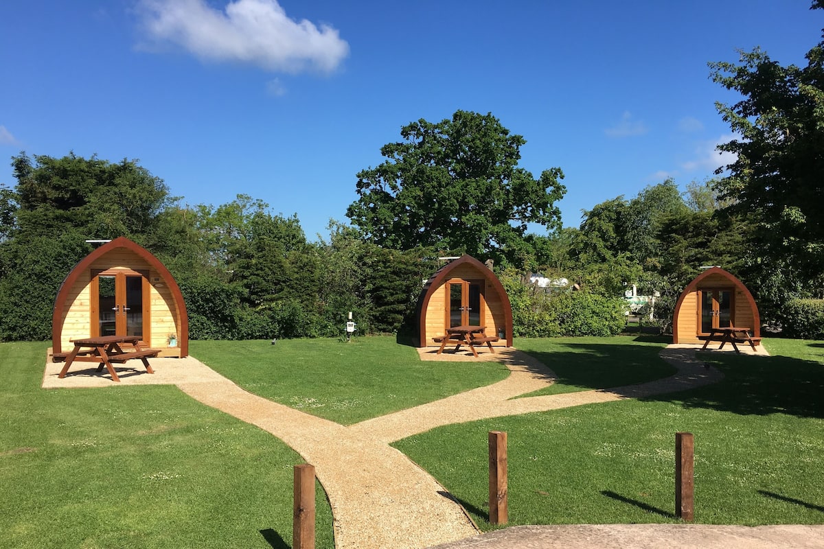 Three wooden arched structures with picnic tables, set in a grassy area with a clear sky.