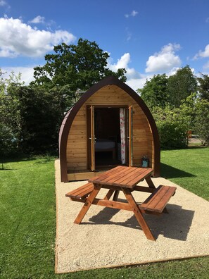 A wooden cabin with an open door, a picnic table, and a gravel area. - Briarfields Glamping Pods (Cheltenham)