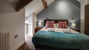 A bedroom with a sloped ceiling, a large bed with a teal bedspread, two bedside tables with lamps, and a radiator.