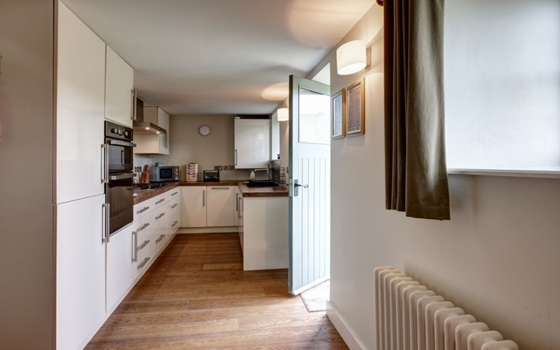 A narrow kitchen with white cabinets, a built-in oven, and a microwave.