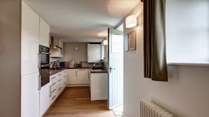 A narrow kitchen with white cabinets, a built-in oven, and a microwave.