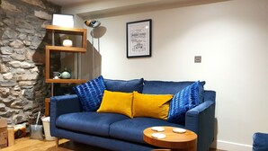 A living room with a blue sofa, wooden side table, and a stone wall.