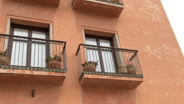 A building with multiple balconies, each with potted plants. There is a signboard with a list of food items. - La Encina Azul Rooms (Ponferrada)