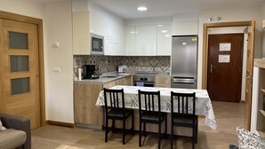 A compact kitchen with a dining area, wooden cabinets, a built-in microwave, a coffee machine, and a refrigerator. - La Encina Azul Rooms (Ponferrada)
