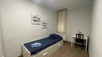 A small, neatly arranged bedroom with a single bed, a desk, and two wall-mounted flower paintings.