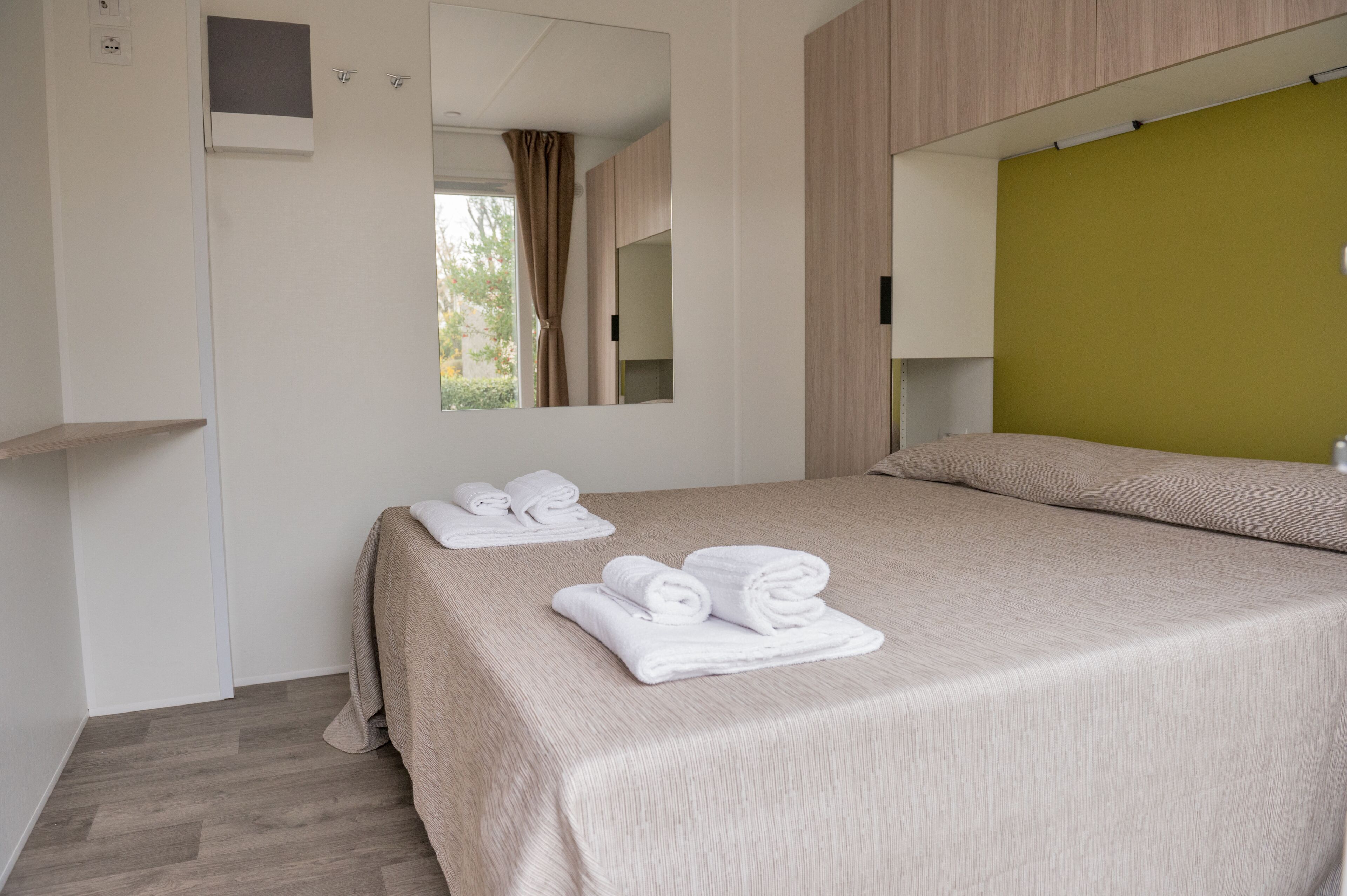 A neatly made bed with white linens, a window with a curtain, and a mirror on the wall.