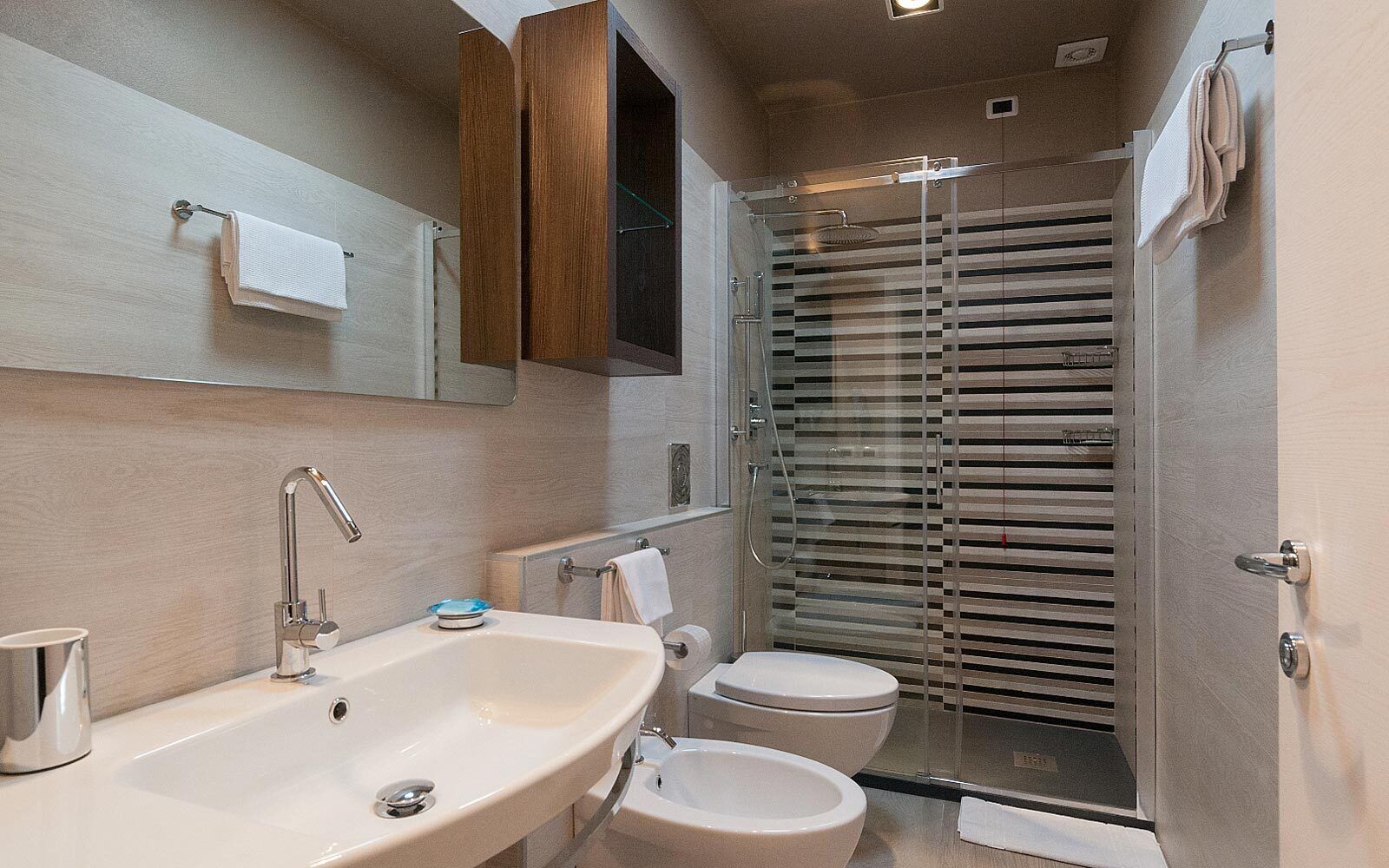Un baño moderno con un lavamanos grande, dos inodoros, una ducha con mampara de vidrio y un armario de madera.