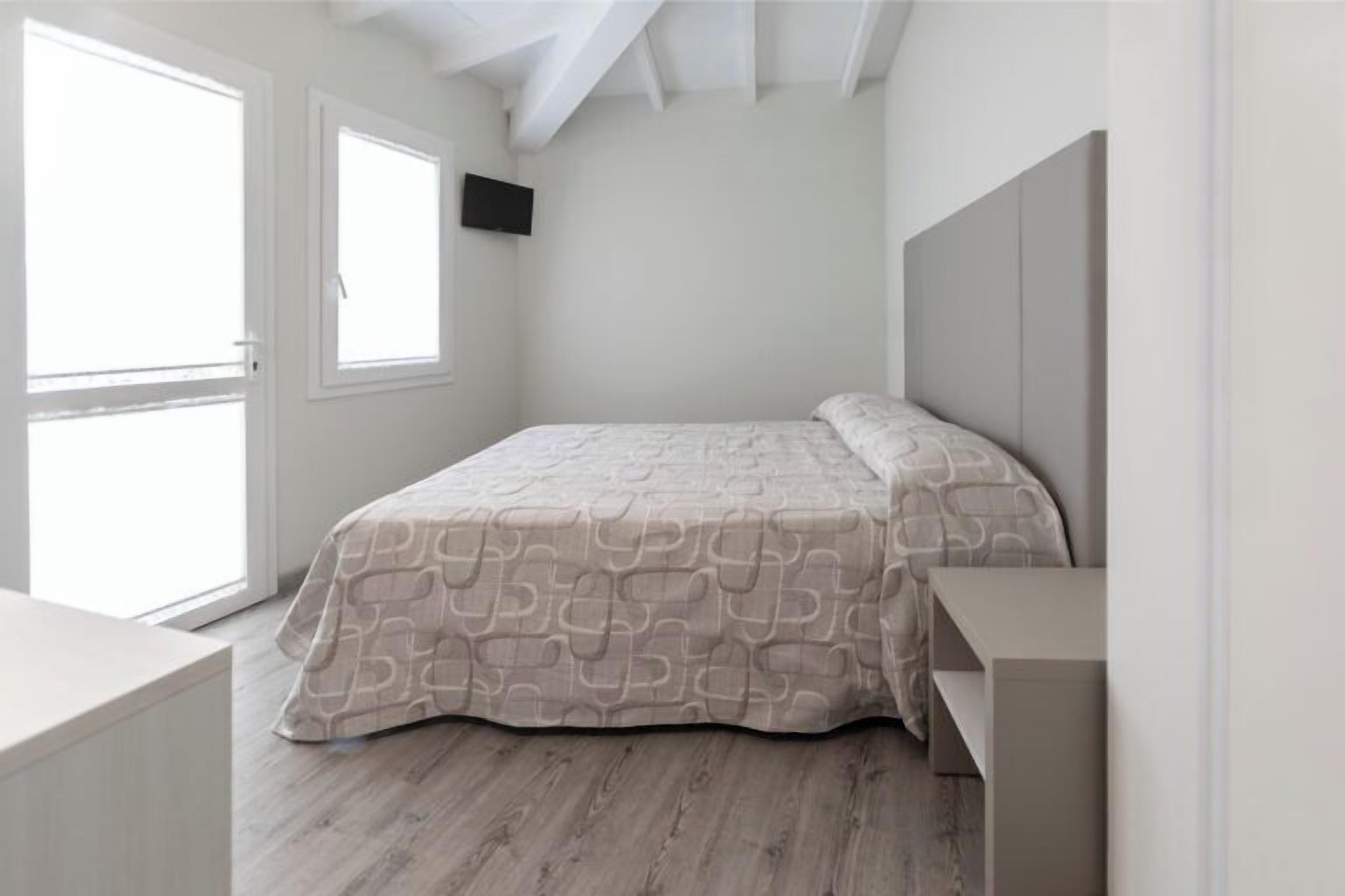 A bedroom with a bed, a TV on the wall, and a large window.