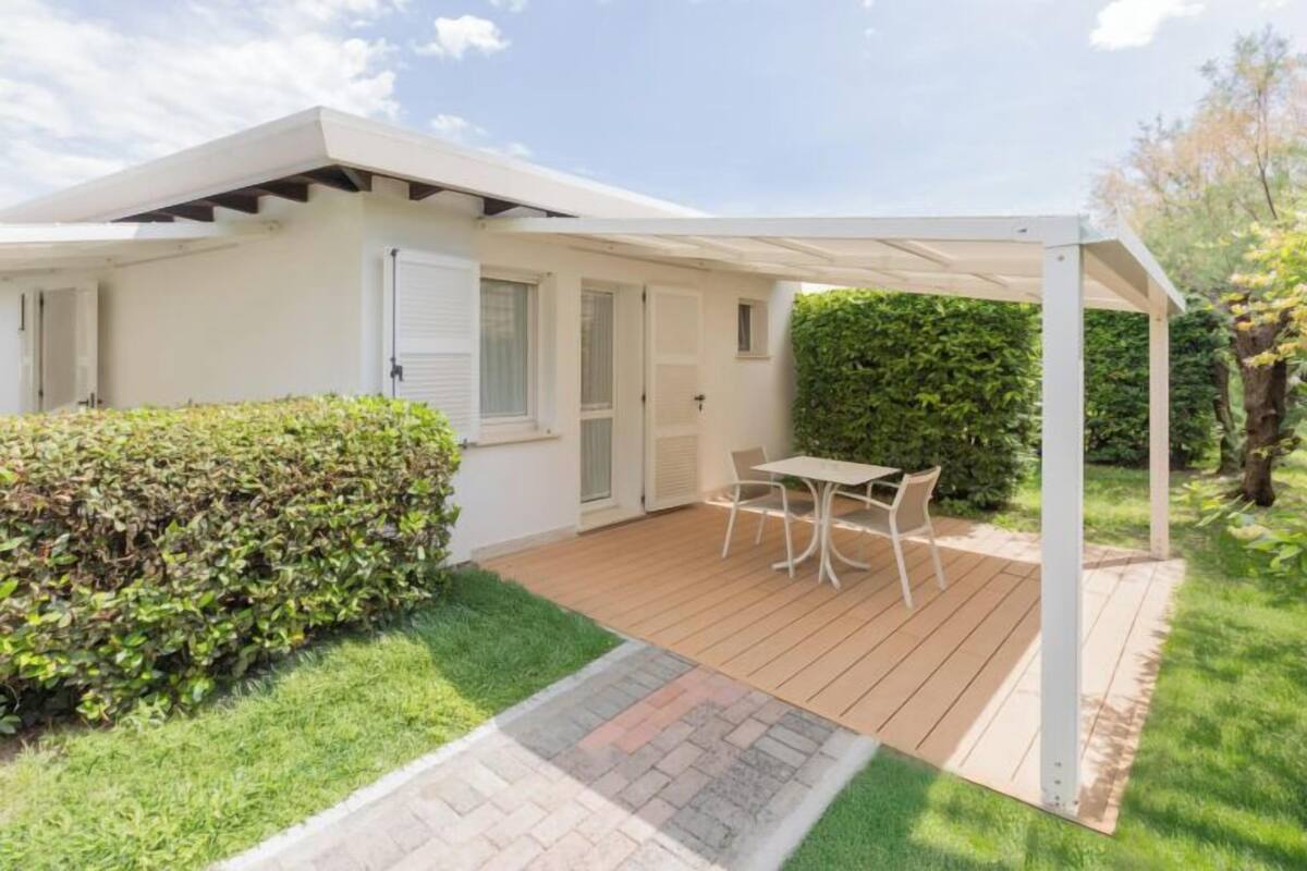 A covered patio area with a table and chairs, surrounded by a hedge and a wooden deck.