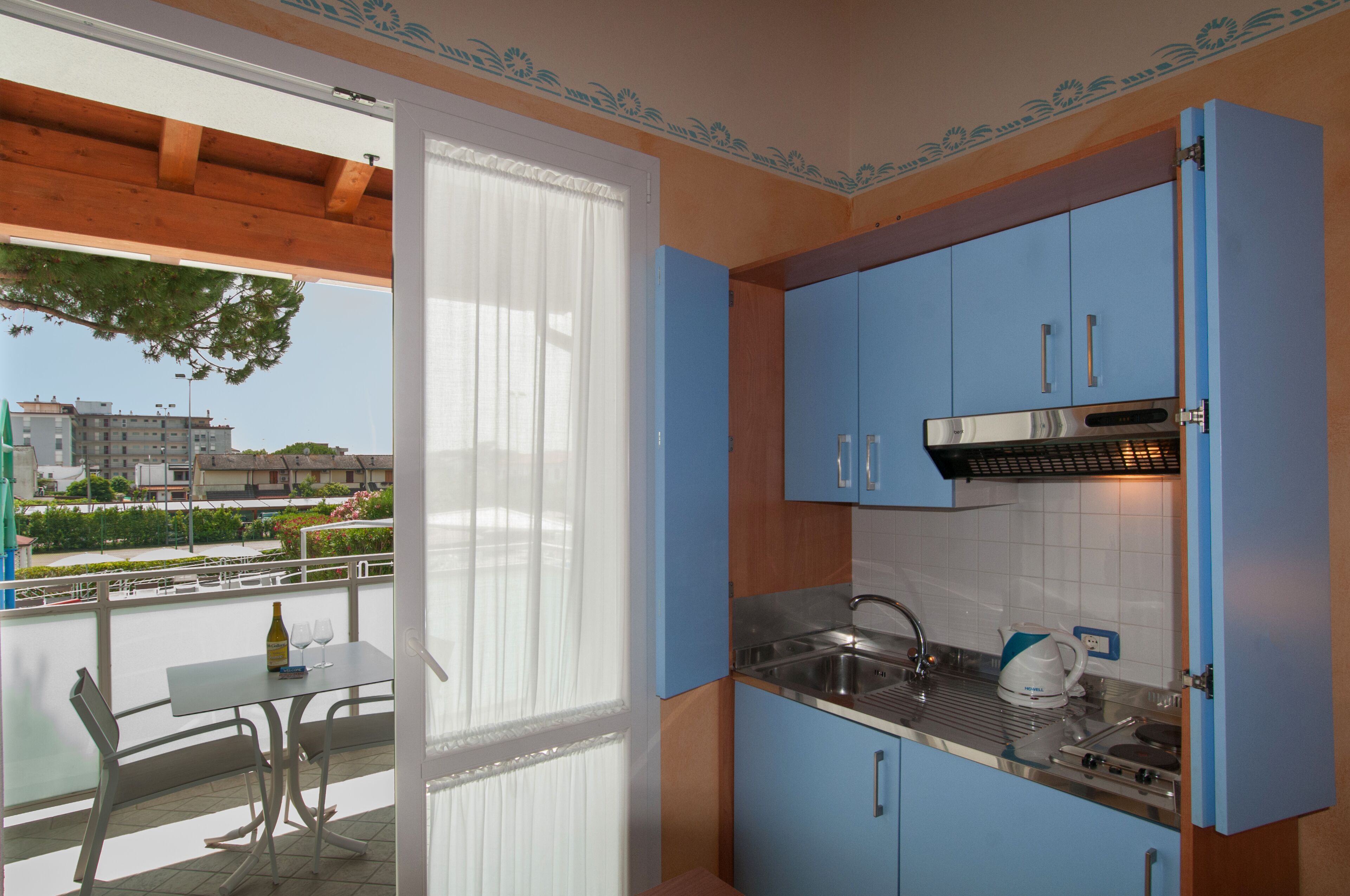 A kitchen with blue cabinets, a stainless steel sink, and a window overlooking a balcony.