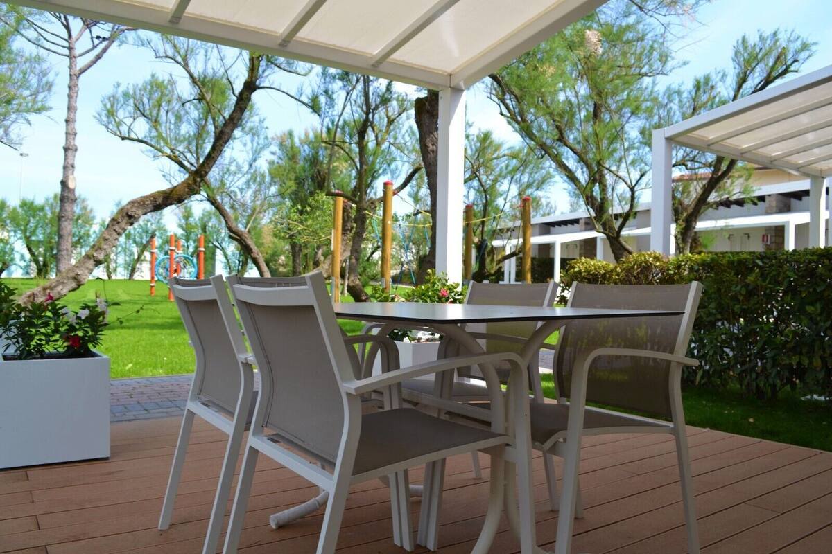 An outdoor patio with a table and chairs, surrounded by greenery and trees.