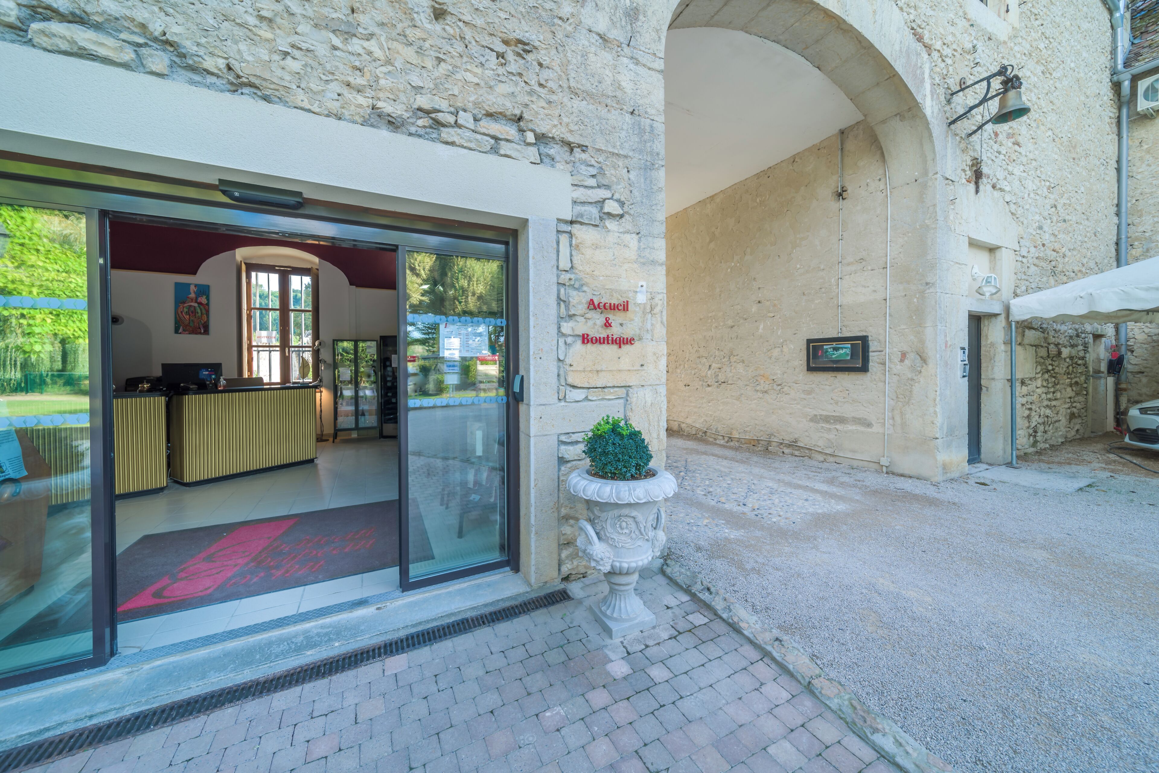 Entrada de un hotel boutique con una recepción, una planta en maceta y una pared de piedra.