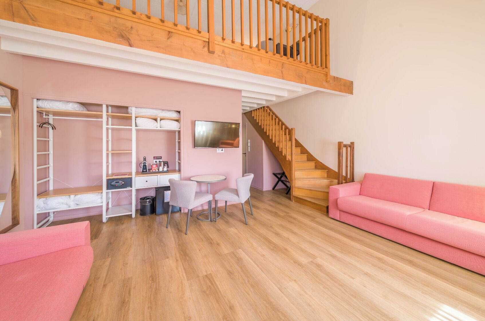 A cozy room with bunk beds, a desk, chairs, a pink sofa, and a staircase.