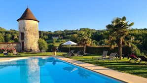 Una piscina amb gandules i una torre de pedra en un jardí exuberant.