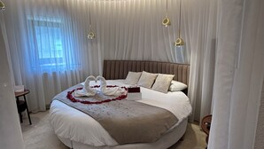 Un llit rodó amb un capçal marró, roba de llit blanca i un ram de flors blanques.