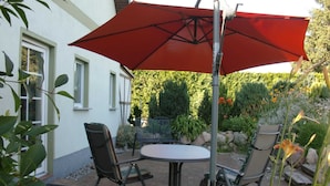 An outdoor patio with a table and chairs, a red umbrella, and a garden with various plants and flowers. - 89820 Fw 2 - 89820 Holiday apartment 2 (Malchow)