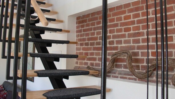 A spiral staircase with wooden steps and black handrails, leading to a brick wall with a decorative wreath. - 89820 Fw 2 - 89820 Holiday apartment 2 (Malchow)