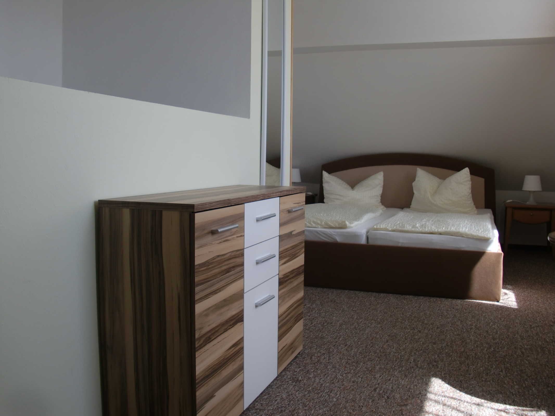 A bedroom with a bed, a nightstand, a dresser, and a mirror.