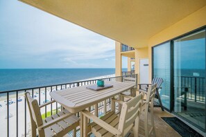 A balcony with a table and chairs, overlooking a beach with umbrellas and a clear view of the ocean. - **WEEKLY SPECIALS!** Phoenix V - 2 Bedroom with Reserved Parking (Orange Beach)