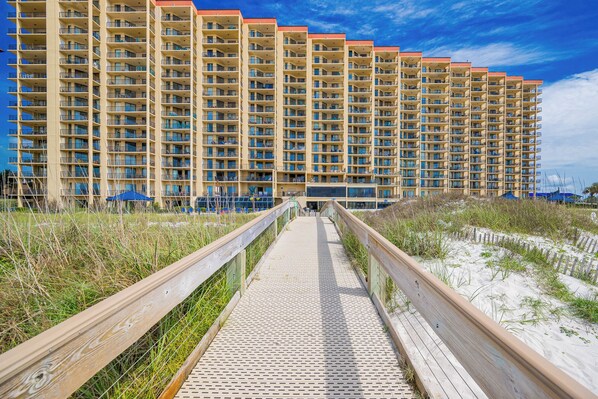 Una larga y estrecha pasarela de madera que conduce a un hotel grande de varios pisos, con balcones.