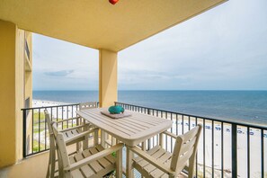 A balcony with a table and chairs overlooking a beach.