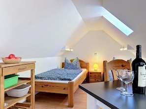 A cozy bedroom with a sloped ceiling, a wooden bed, a bedside table with a lamp, a wine bottle, and a bowl of fruit.