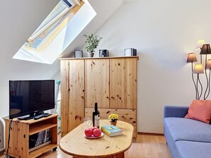 A modern living room with a television, wooden cabinet, table with books and apples, and a sofa.