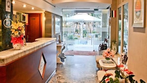 Ein Hotel-Empfangsbereich mit einer Marmor-Theke, gerahmten Bildern und Blick auf den Außenbereich durch Glastüren.