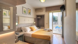 Ein Hotelzimmer mit einem großen Bett, Nachttischen, einem an der Wand montierten Fernseher und einem Balkon mit Gartenmöbeln.