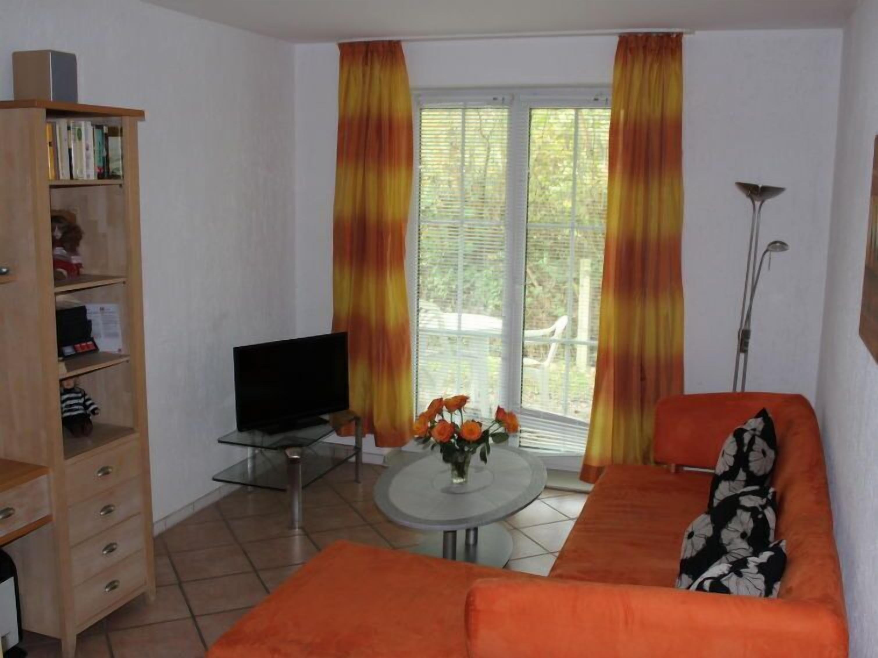 A living room with a sofa, a television, a bookshelf, and a window with curtains.