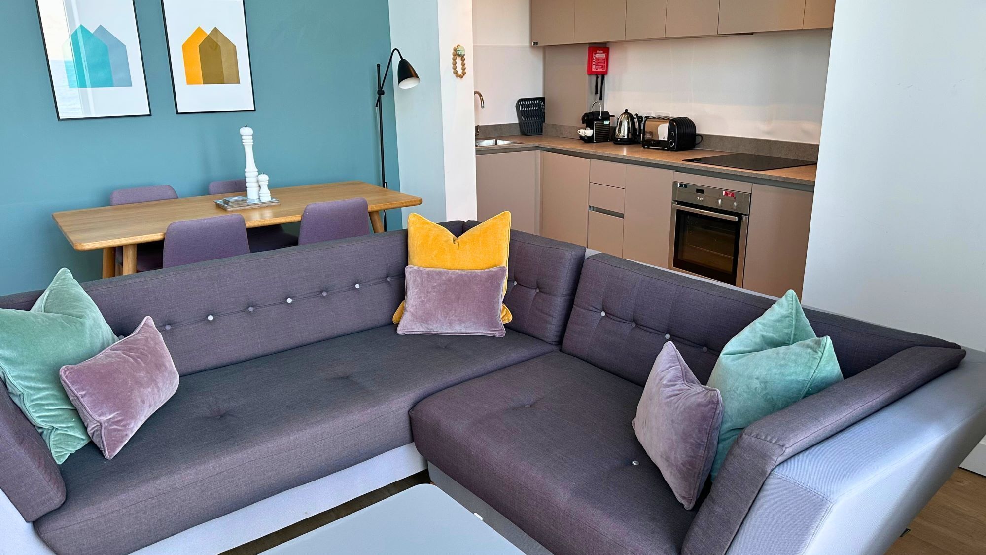A modern living room with a sectional sofa, a dining table, and a kitchen area.