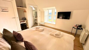 Ein Hotelzimmer mit Bett, Kissen, Fernseher, einem kleinen Tisch mit Tee-Service und einem Fenster mit Aussicht.