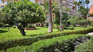 A well-maintained garden with palm trees and hedges in front of a multi-story building with balconies.