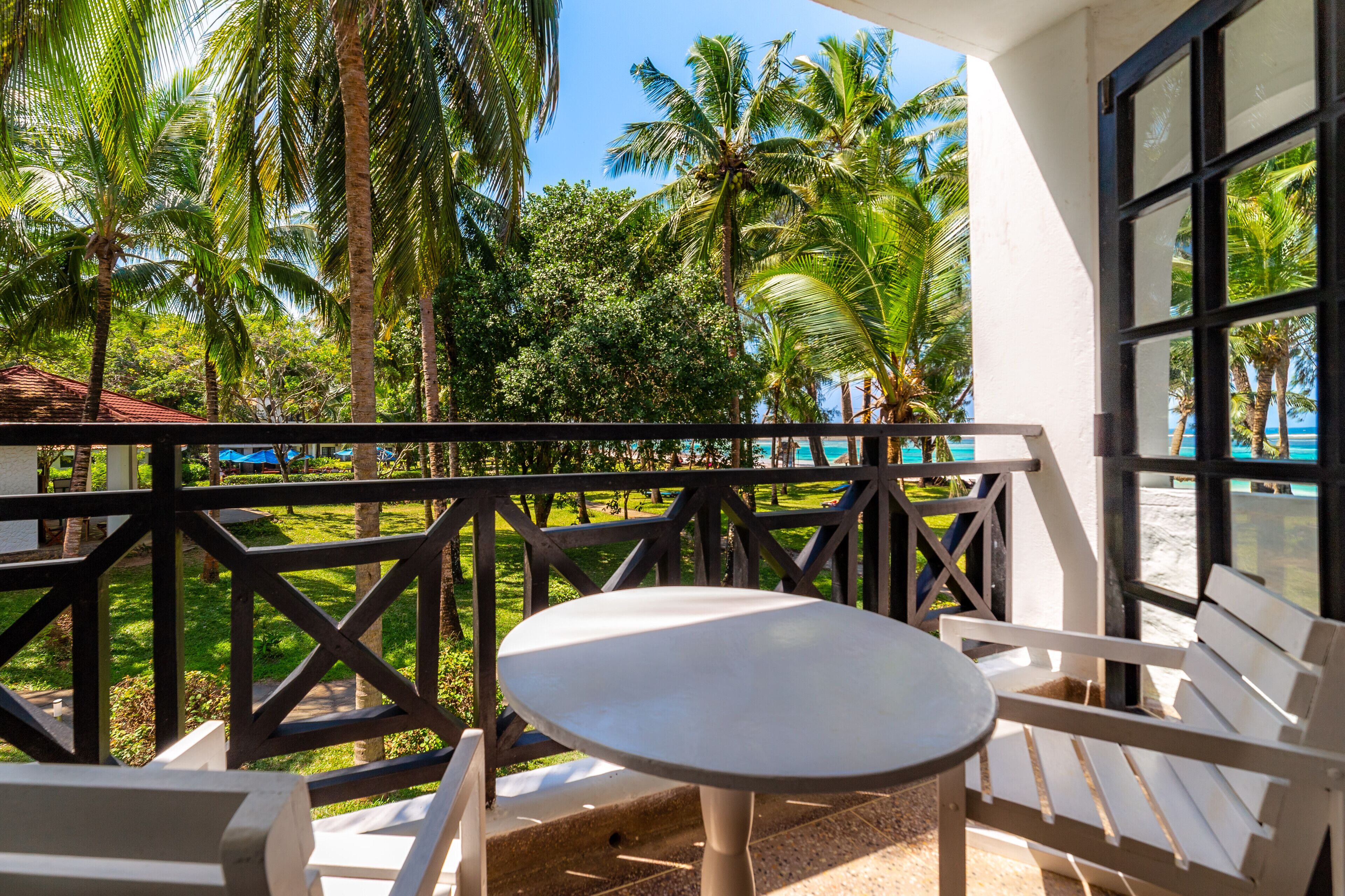 Un balcón con una mesa y sillas, con vista a una piscina y palmeras.