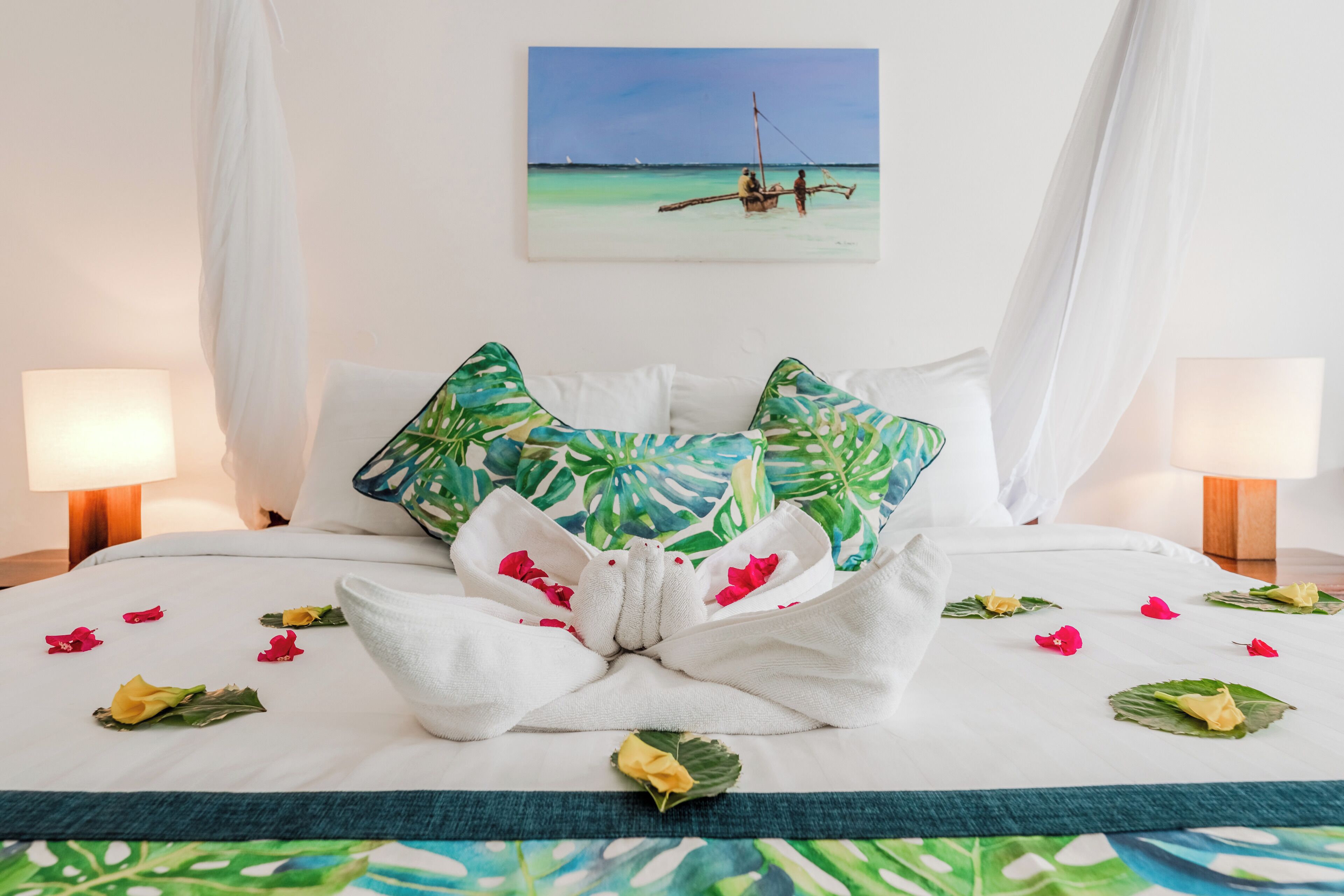 Un llit ben fet amb una almoinada de temàtica tropical, una tovallola decorativa i flors disperses.