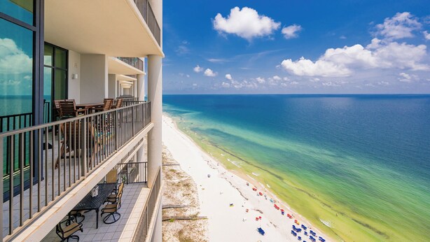A hotel balcony with outdoor seating overlooking a beach and ocean.