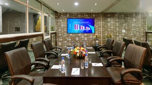 Une salle de conférence avec une longue table, des fauteuils en cuir marron, un arrangement floral au centre et un écran affichant un graphique à barres.