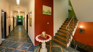 Un couloir d’hôtel avec un sol en marbre, un escalier orné d’un mur vert et une fontaine décorative.