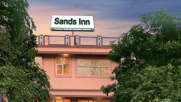 Un hôtel appelé Sands Inn, avec une enseigne au-dessus de l’entrée, un chemin pavé et des plantes en pot disposées autour du bâtiment.