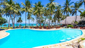 A large pool surrounded by palm trees and lounge chairs, with a view of the ocean. - Diani Sea Lodge (Diani Beach)
