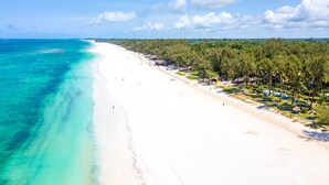 A beach with clear turquoise waters, white sand, and a line of palm trees and beach huts. - Diani Sea Lodge (Diani Beach)