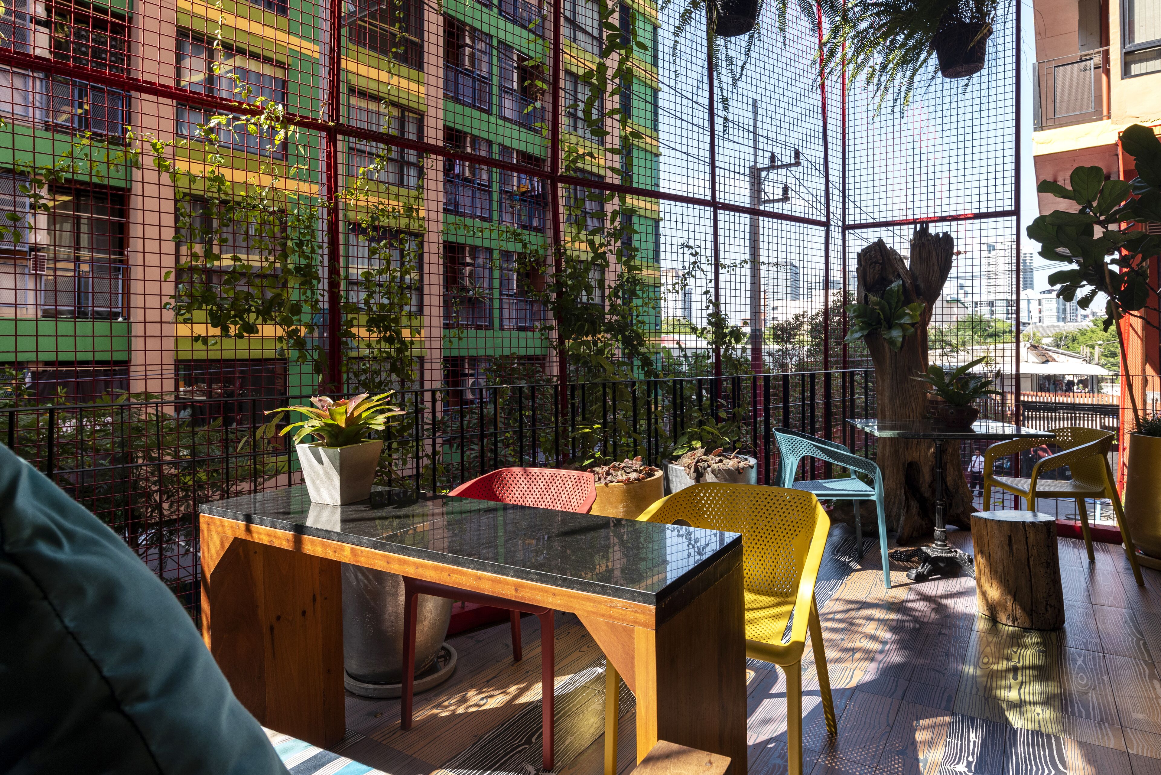 An outdoor seating area with a glass table and chairs, surrounded by a metal fence and potted plants.
