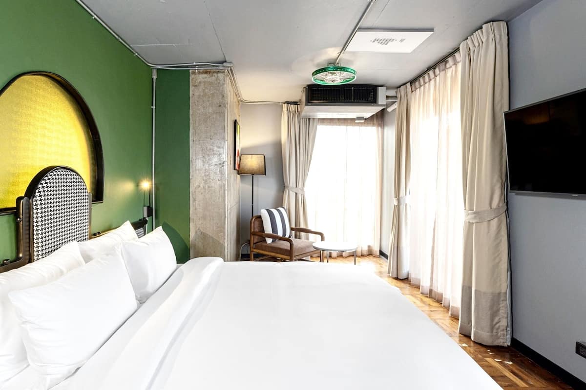 A hotel room with a large bed, a chair, a small table, a lamp, and a TV.