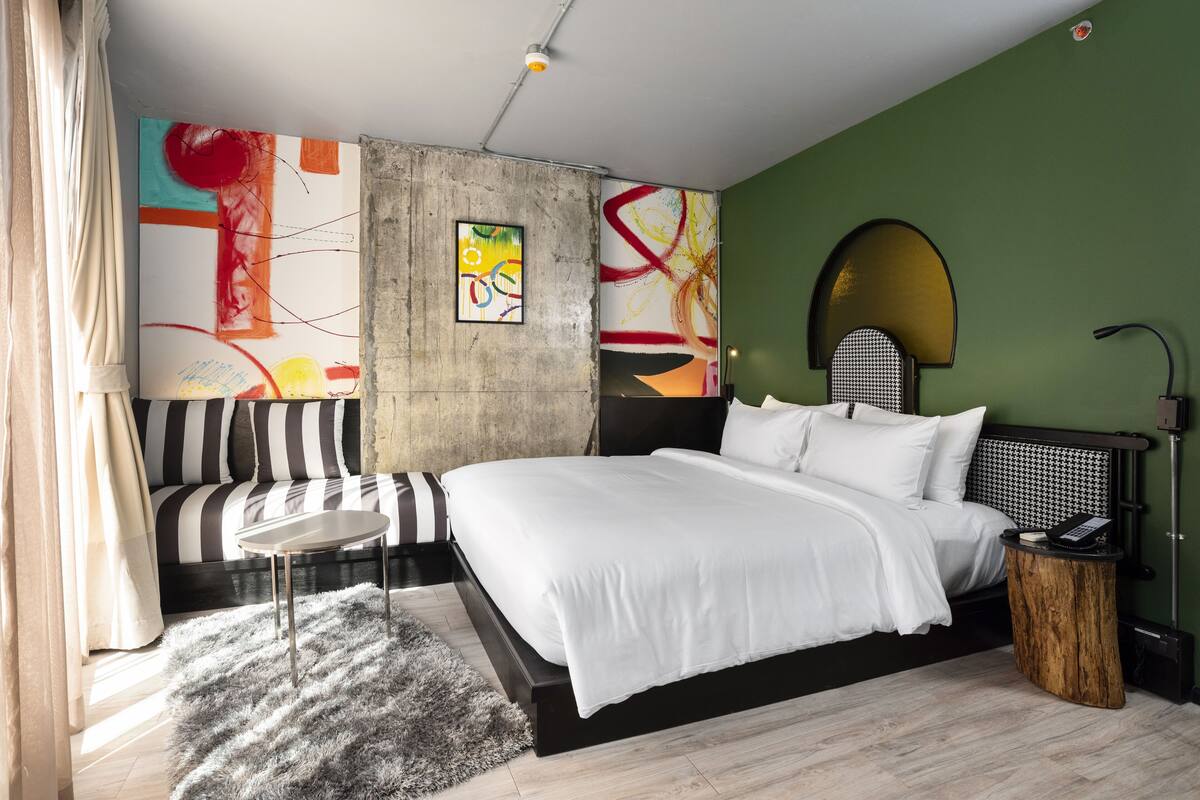 A modern bedroom with a large bed, a sofa, abstract art on the walls, and a unique ceiling light fixture.