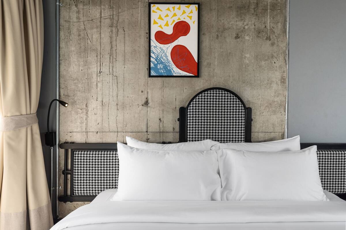 A bed with white linens, a black and white headboard, and a framed abstract artwork on the wall.