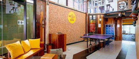 Un gimnasio con mesa de ping pong, bancos de madera y taquillas.