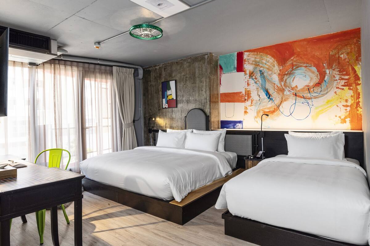 A modern hotel room with a large bed, a desk, and a vibrant abstract painting on the wall.